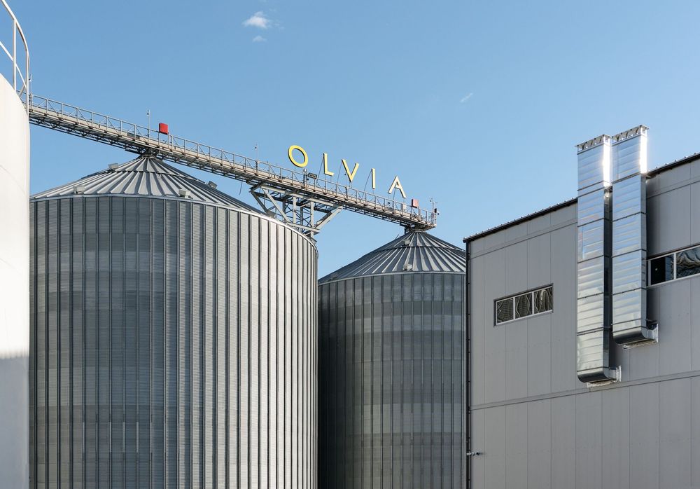 Транспортерна галерея зі знаком OLVIA над силосами, поруч виробничий корпус